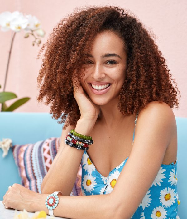 Indoor portrait of African American female with bushy curly hair, sits at table in cafeteria with cocktail, being in high spirit, celebrates starting holidays. People, lifestyle and beauty concept